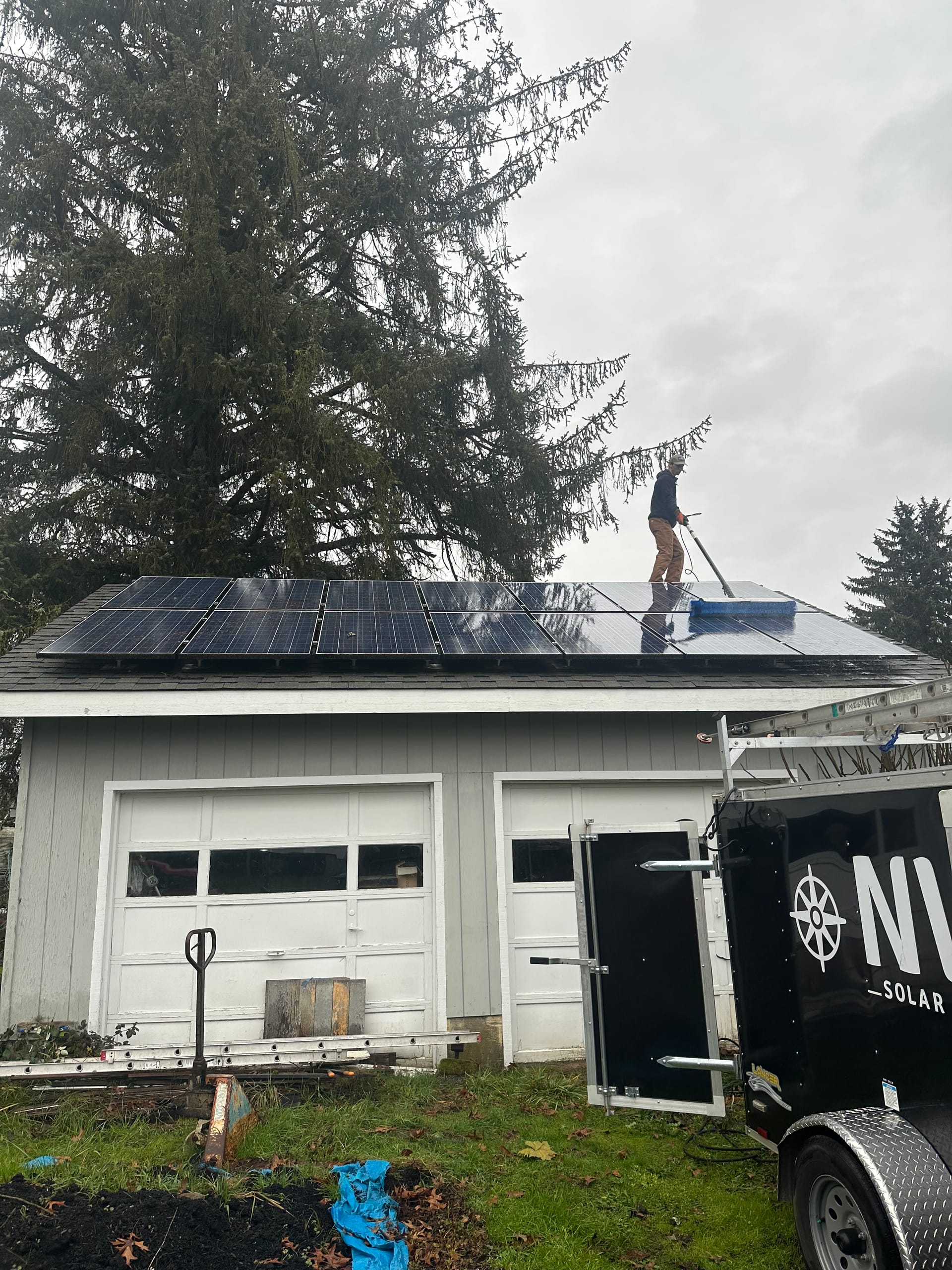 A technician cleaning rooftop solar panels with a rotary brush, the NW Solar Clean trailer alongside